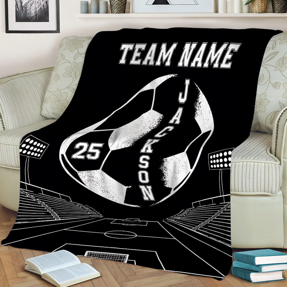 Black soccer throw blanket on a sofa featuring a large soccer ball, stadium seating and field lines