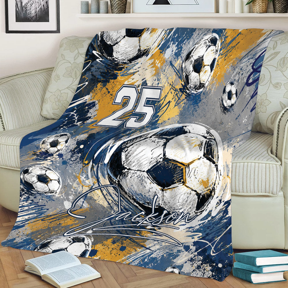Soccer blanket draped over a sofa featuring dynamic navy, gold, gray, and white ball graphics