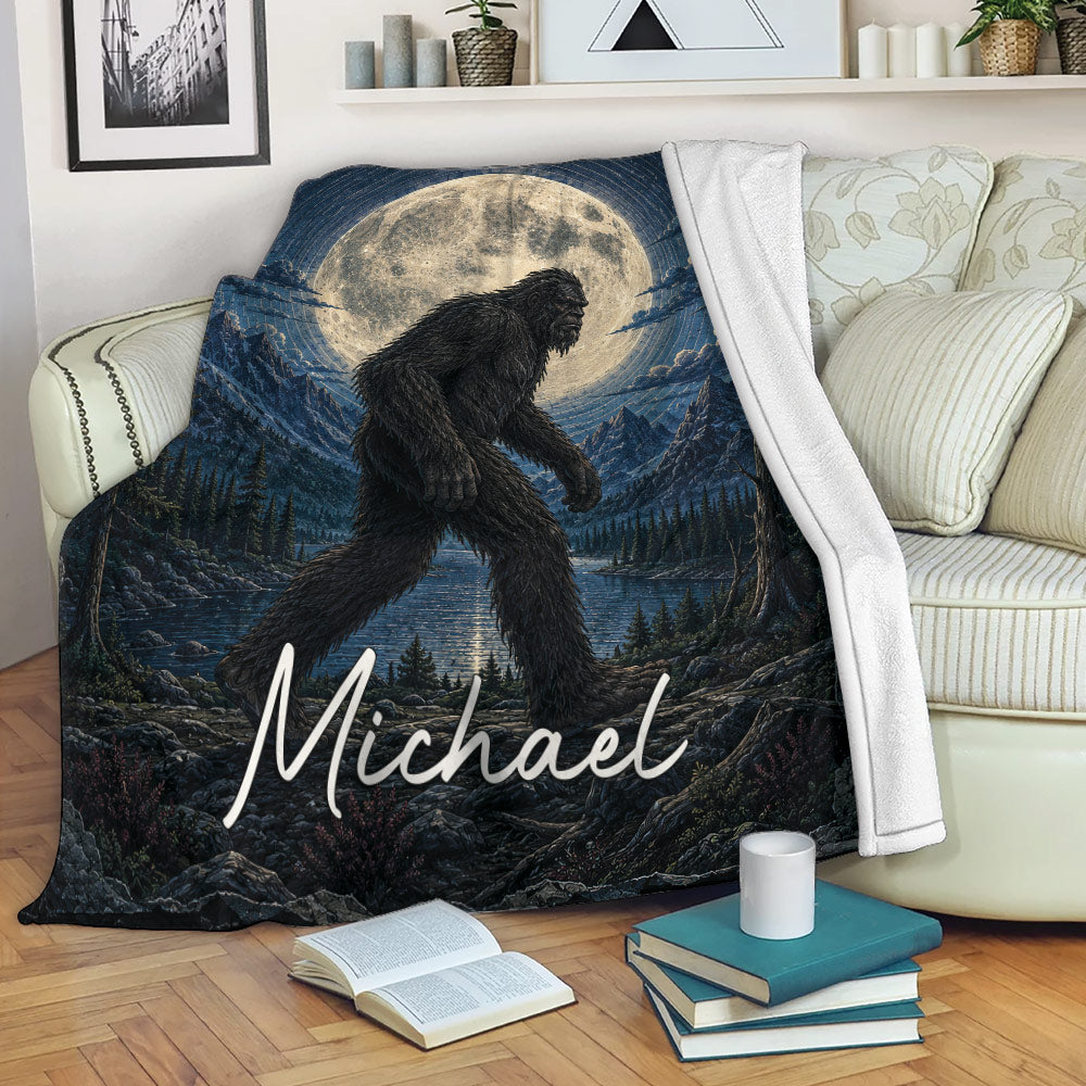 Bigfoot throw blanket displayed on a sofa with moonlit mountain and forest artwork