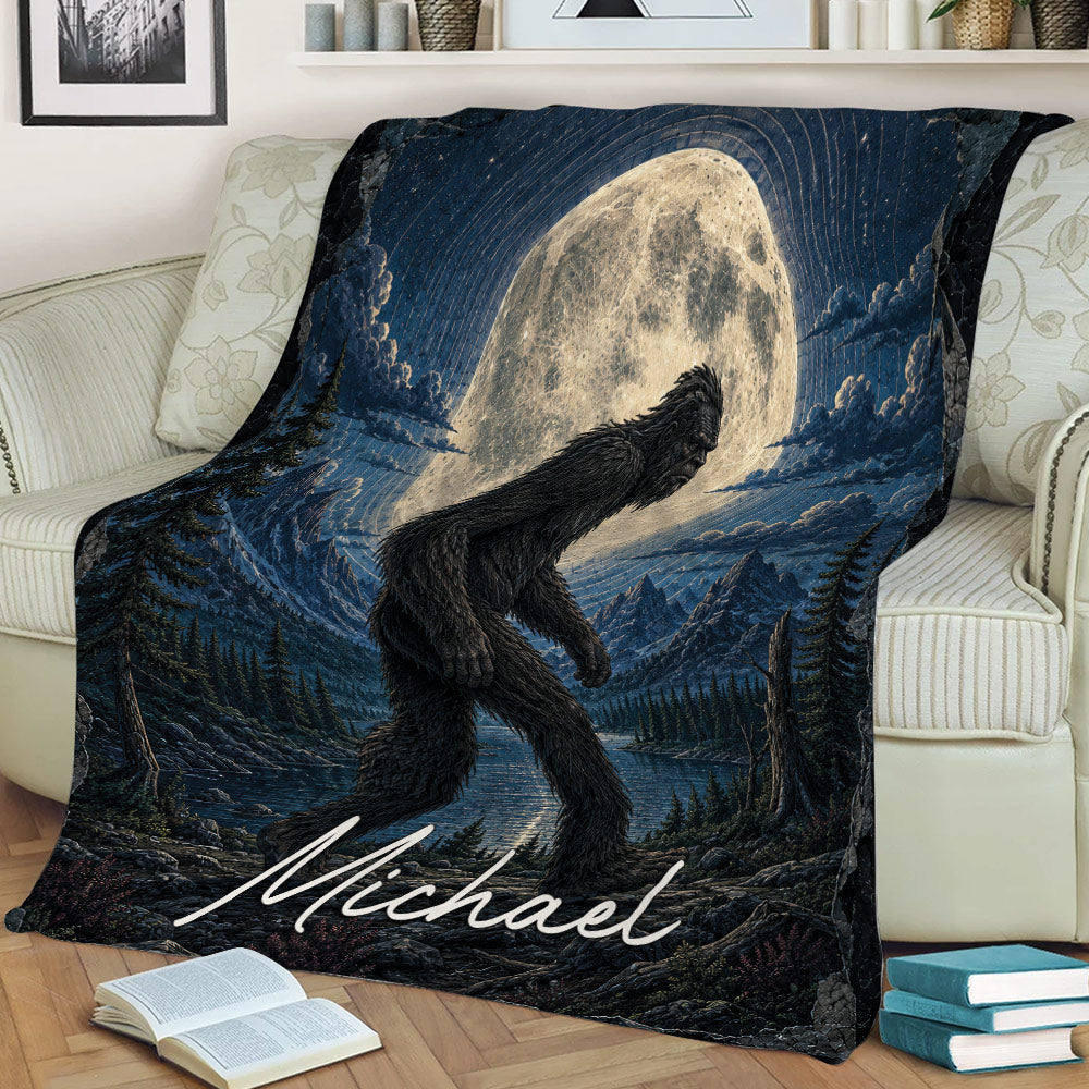 Bigfoot blanket draped over a sofa featuring a full moon, mountains, lake and evergreen forest