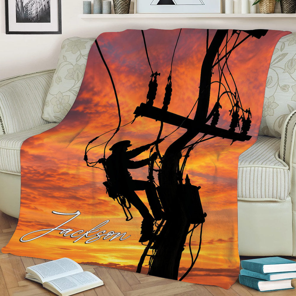 Lineman throw blanket displayed on a couch with power lines, utility worker silhouette, and sunset artwork