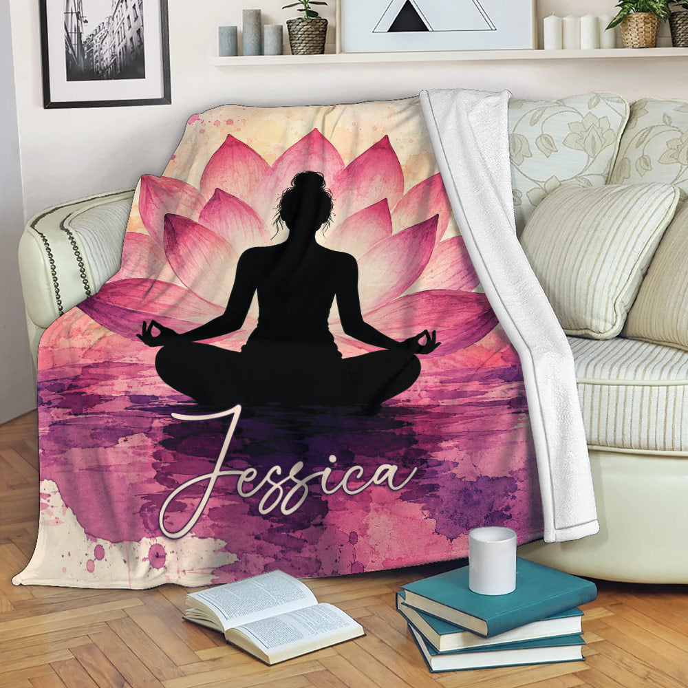 Yoga blanket displayed on a sofa with a meditating figure, pink lotus petals, and artistic watercolor textures