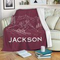 Maroon skiing throw blanket draped over a sofa with mountain and skier artwork