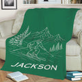 Green skiing throw blanket on a sofa with skier, mountain, and evergreen artwork