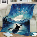 Blue kayak throw blanket displayed on a couch with mountain, pine forest, lake, and paddler artwork