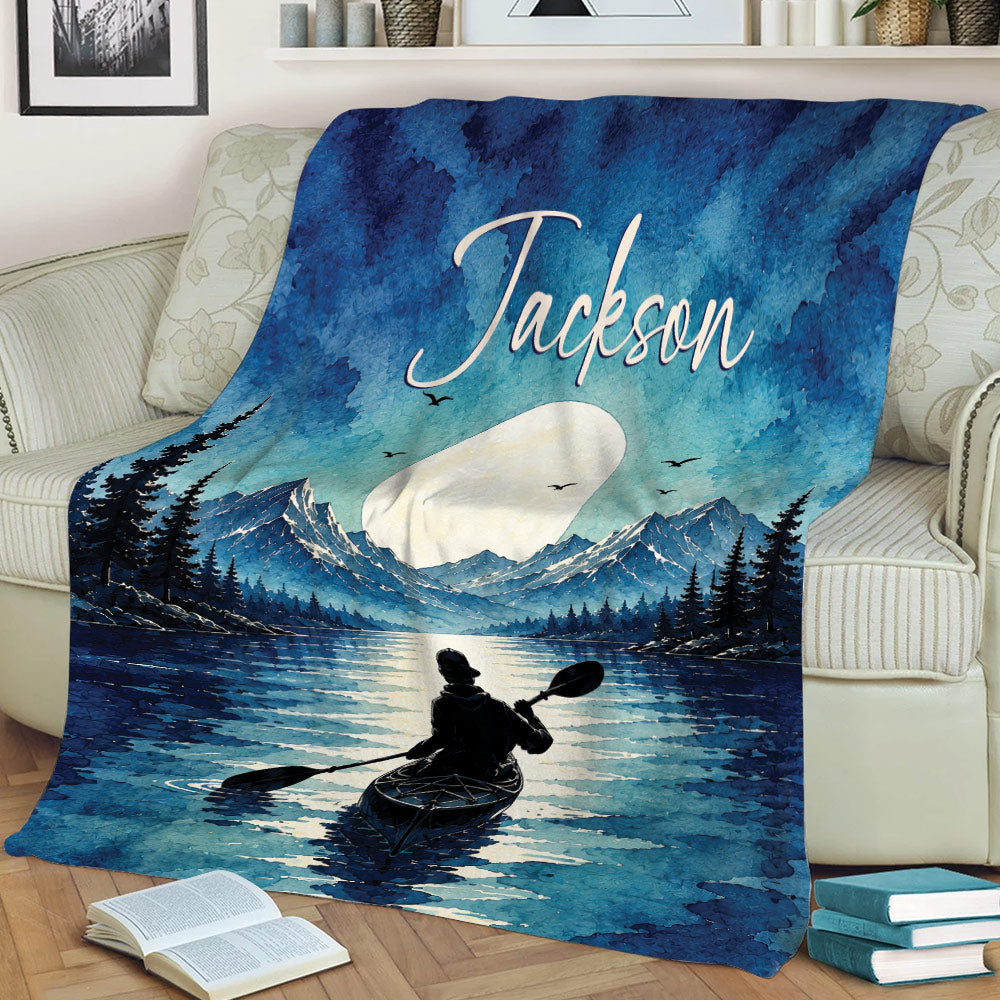 Blue kayak throw blanket displayed on a couch with mountain, pine forest, lake, and paddler artwork