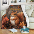 Squirrel throw blanket with autumn woodland artwork draped over a sofa beside books