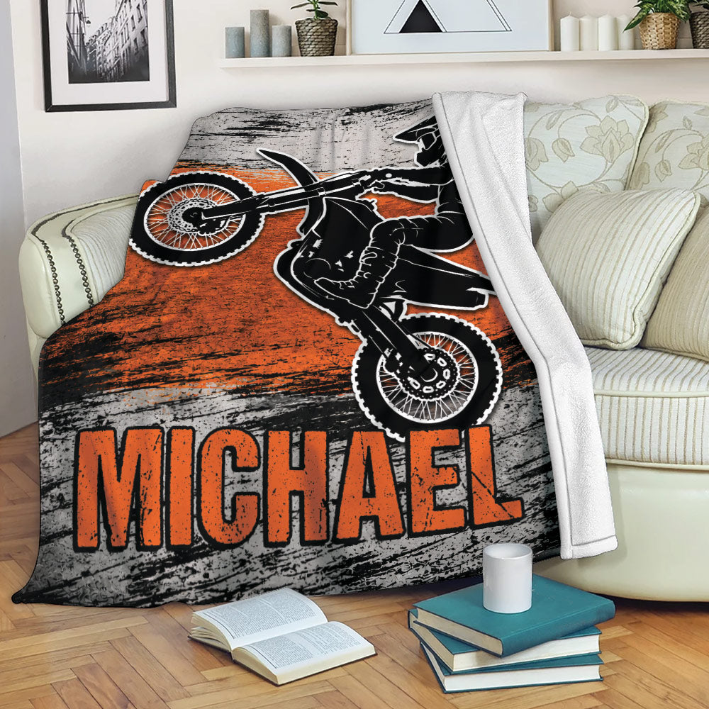 Motocross blanket draped over a sofa with dirt bike rider artwork in an orange and distressed black design