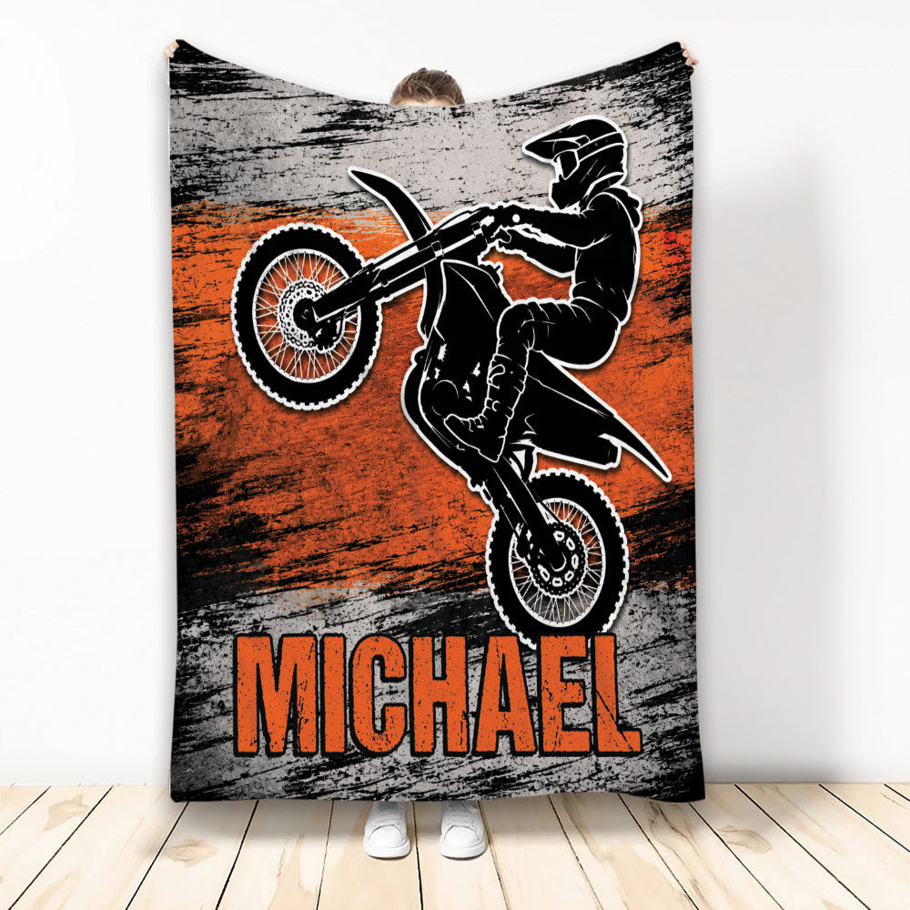 Motocross throw blanket featuring a dirt bike rider performing a jump in bold orange, black, and gray artwork