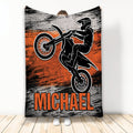 Motocross throw blanket featuring a dirt bike rider performing a jump in bold orange, black, and gray artwork