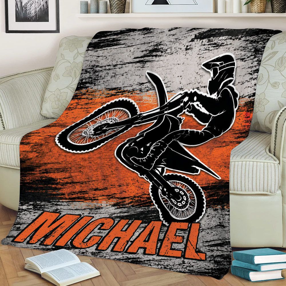 Motocross throw blanket displayed on a couch with dynamic dirt bike rider and rugged orange graphic design