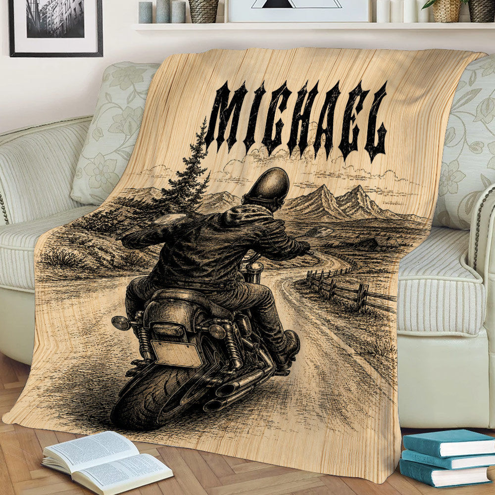 Biker blanket draped over a sofa showing a motorcycle rider, winding road, trees, and mountains