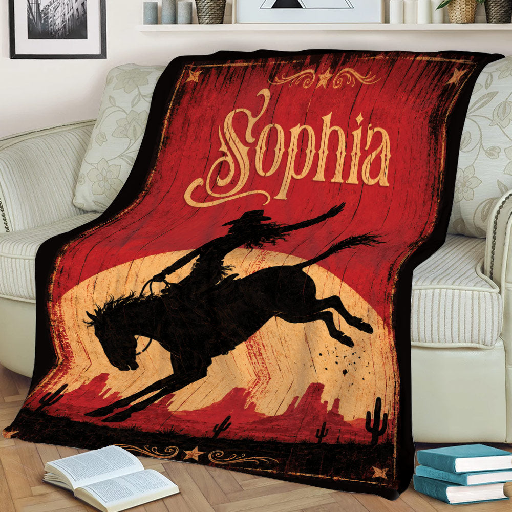 Western cowgirl blanket displayed on a couch with bucking horse and desert sunset artwork