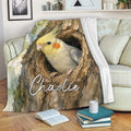 Cockatiel throw blanket displayed on a sofa with detailed watercolor bird and tree artwork
