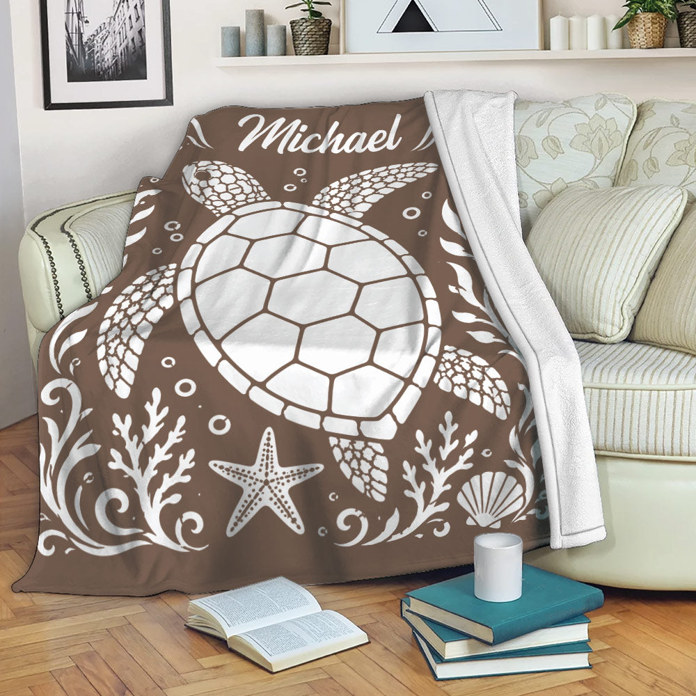 Brown sea turtle blanket draped over a sofa with coastal artwork and a cozy reading area