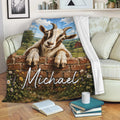 Goat blanket draped over a sofa with a horned goat, brick wall, wildflowers, and rustic farmhouse scenery