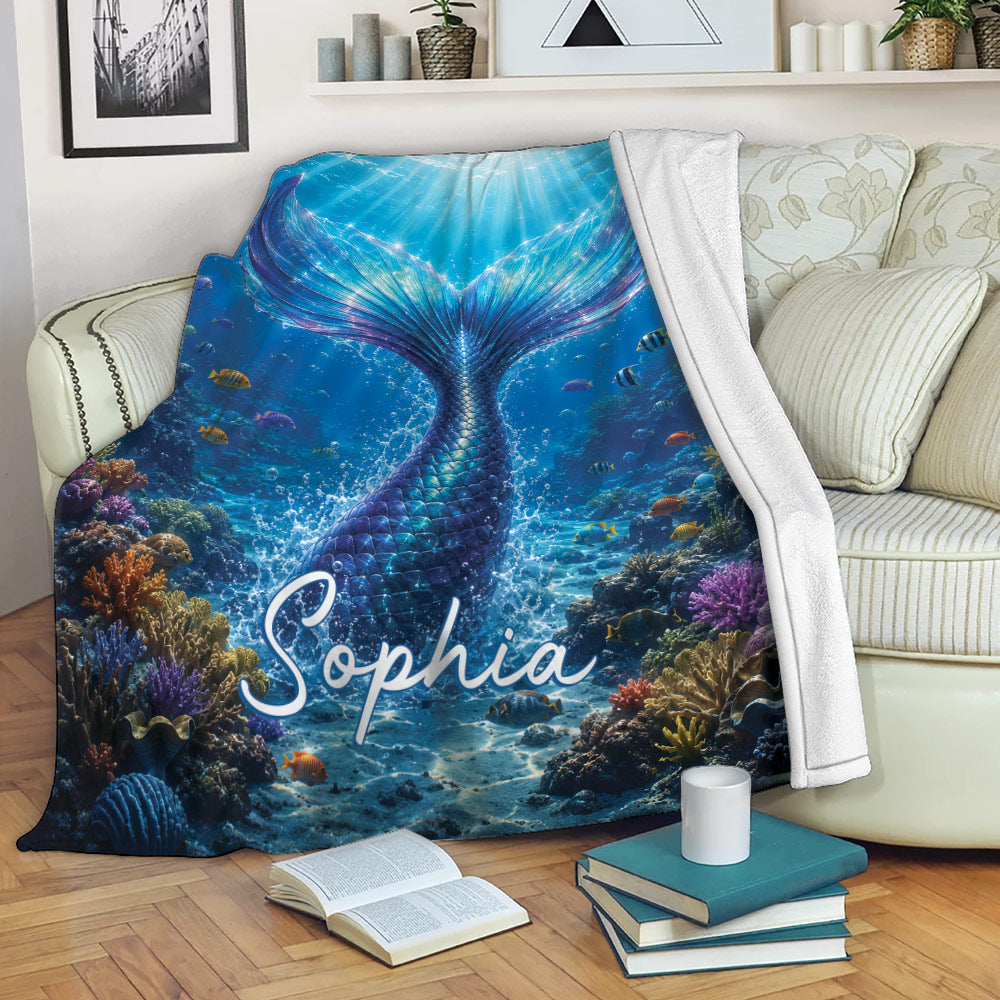 Mermaid throw blanket draped over a sofa with a blue underwater tail and colorful coral reef artwork