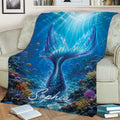 Blue mermaid throw blanket displayed on a sofa with a luminous tail, tropical fish, and coral reef scene