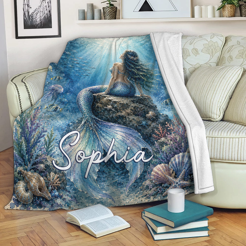 Mermaid throw blanket draped over a sofa, showing blue underwater artwork and colorful ocean life