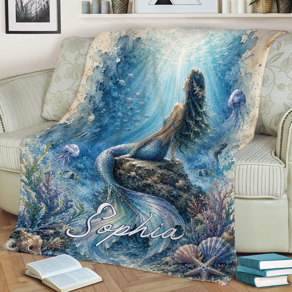 Mermaid throw blanket displayed on a couch with an underwater fantasy scene, coral, fish, and seashells