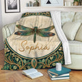 Dragonfly throw blanket draped over a sofa with teal, gold and cream botanical artwork