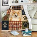 Corgi blanket draped over a sofa with plaid panels, paw prints, and warm rustic colors