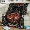 Decorative ladybug blanket featuring red patterned wings, flowers, and dark botanical artwork on a sofa
