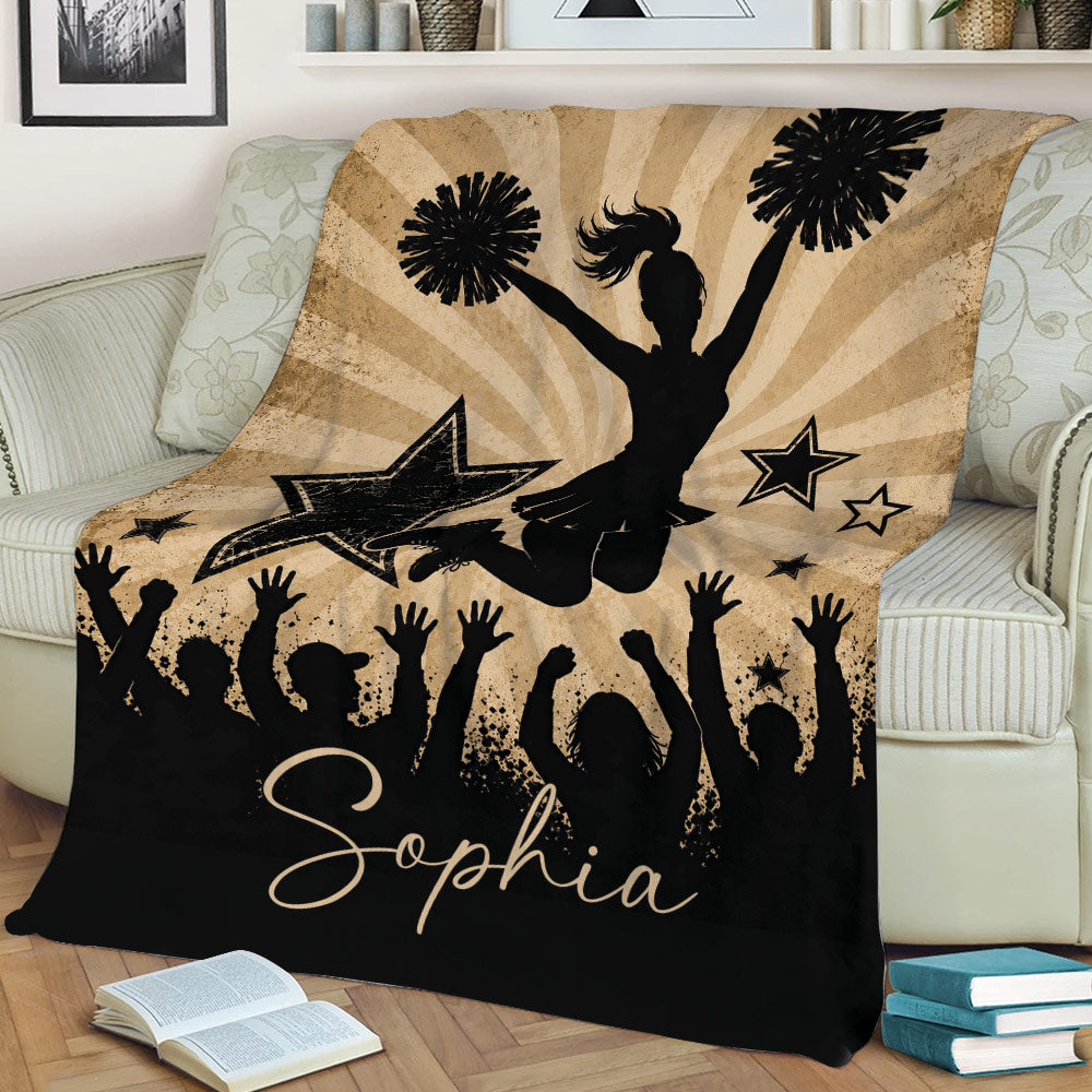 Cheerleading throw blanket styled on a couch with bold black silhouettes, pom-poms, stars, and celebration artwork