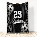 Black and white soccer blanket displayed vertically with soccer balls and goal net artwork