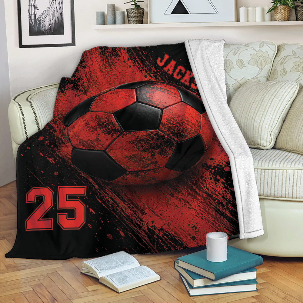 Red and black soccer blanket draped over a sofa with large soccer ball artwork and bold sports graphics