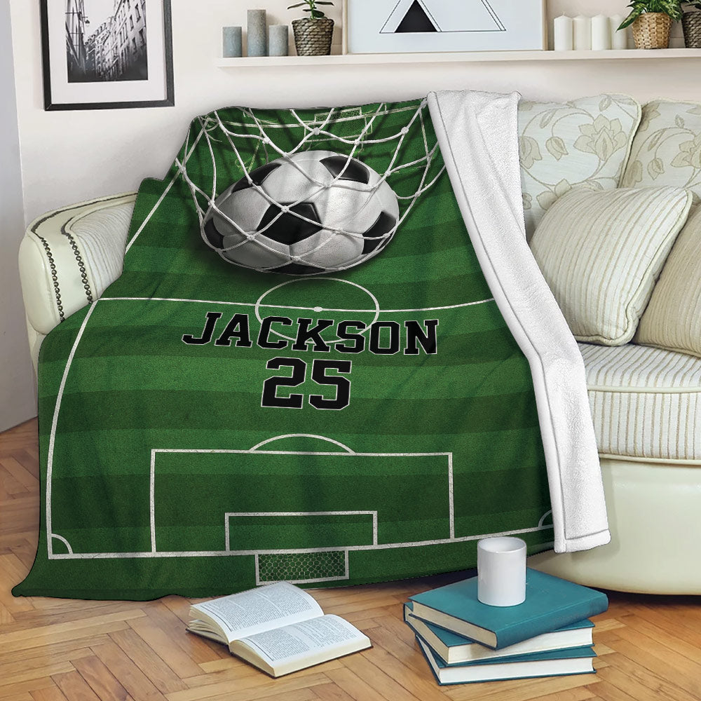 Soccer throw blanket draped across a sofa with green field markings and goal artwork