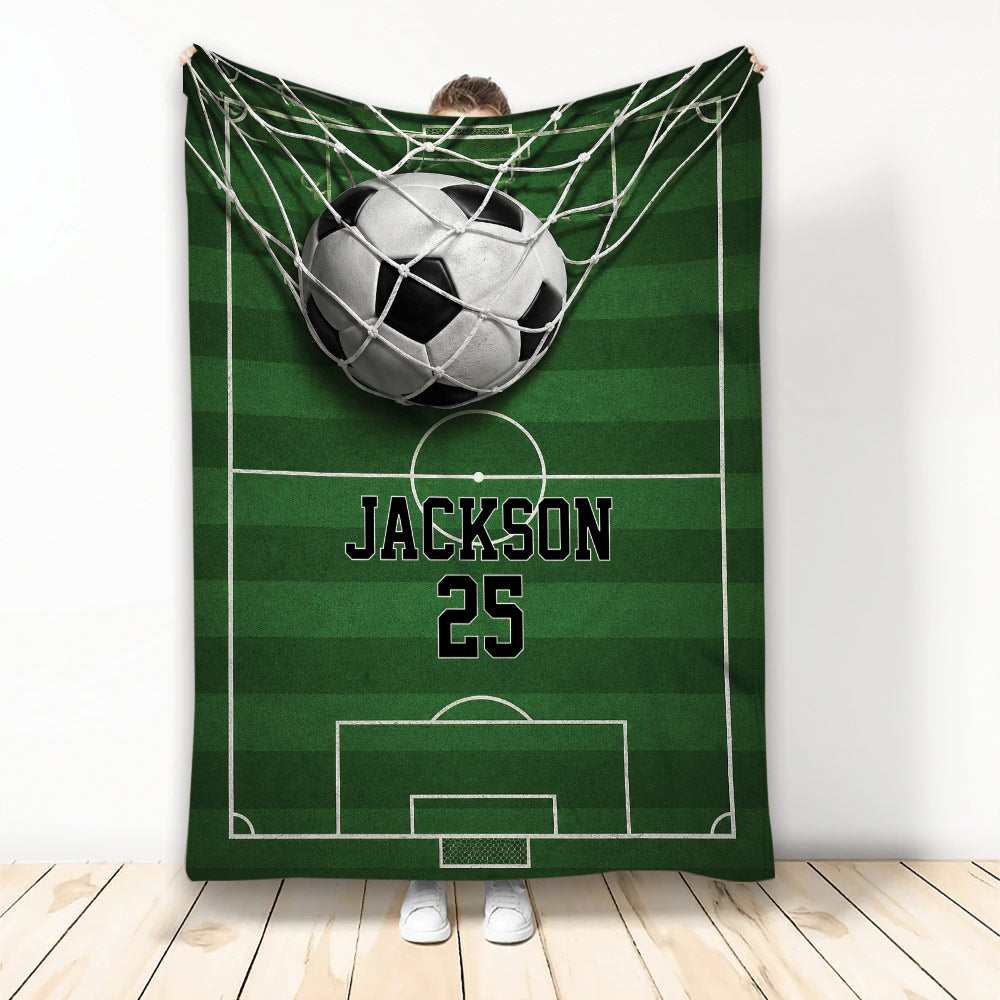 Soccer blanket displayed vertically with a ball in the goal net over a green field design