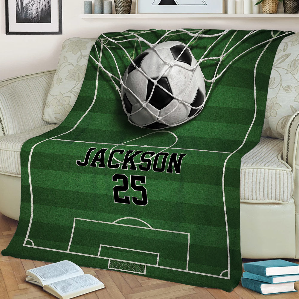 Soccer blanket spread over a sofa featuring a ball in the net and green pitch design