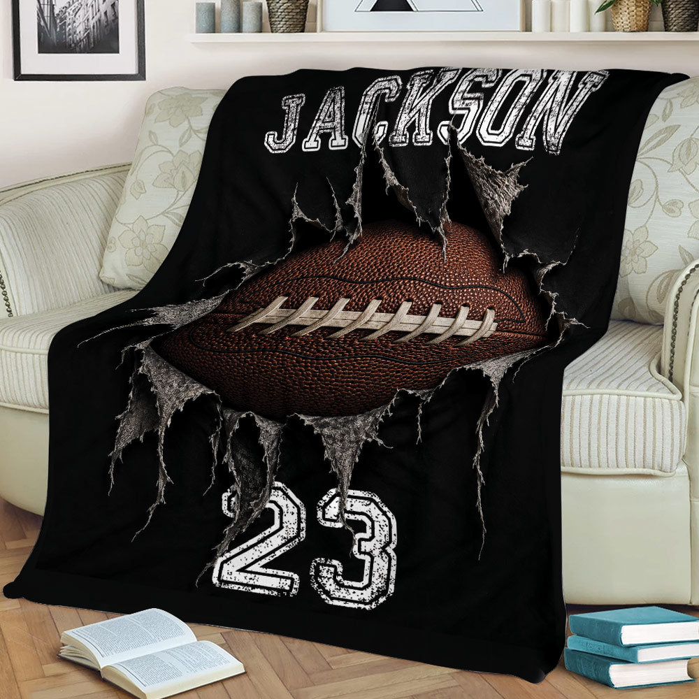 Black football blanket draped over a sofa, featuring a close-up football bursting through ripped fabric