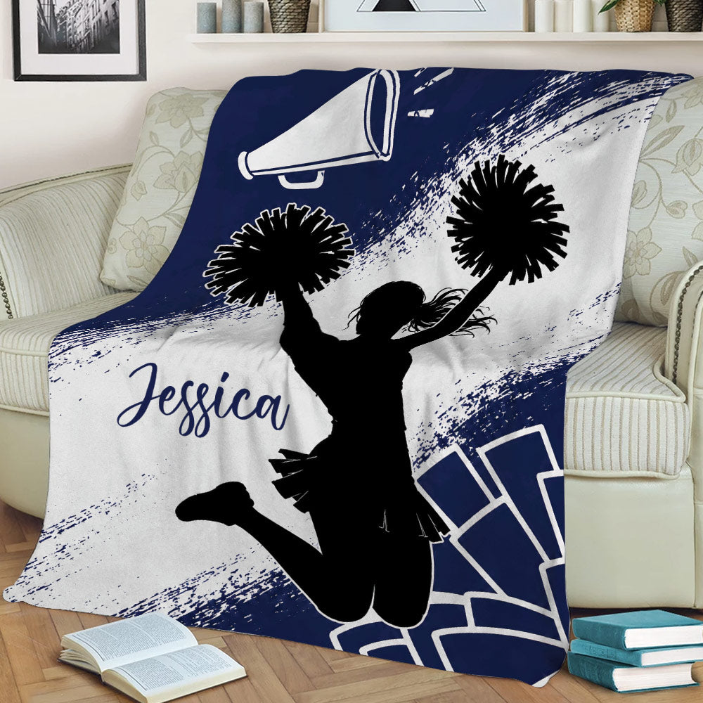 Cheerleading throw blanket displayed on a couch with pom-poms, megaphone, and bold navy and white artwork