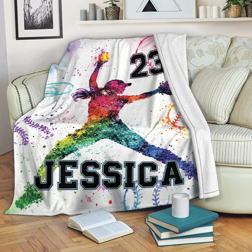 Softball throw blanket draped over a couch with colorful female player artwork and softball-themed splatter design