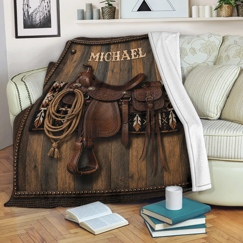 Western cowboy throw blanket draped across a sofa with saddle, rope, leather tack, and rustic wood artwork