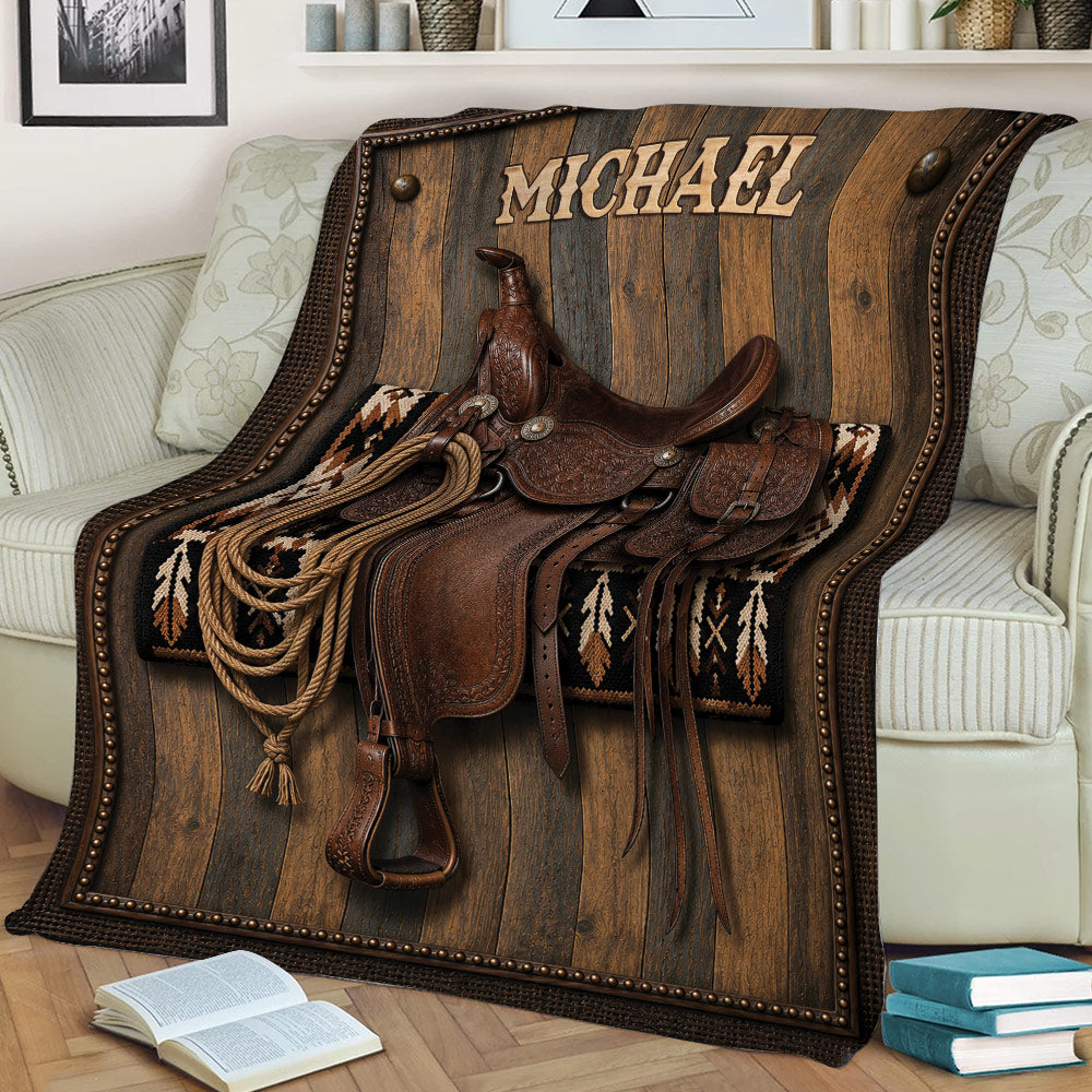 Close view of a cowboy throw blanket displaying a detailed Western saddle, rope, leather gear, and rustic decor