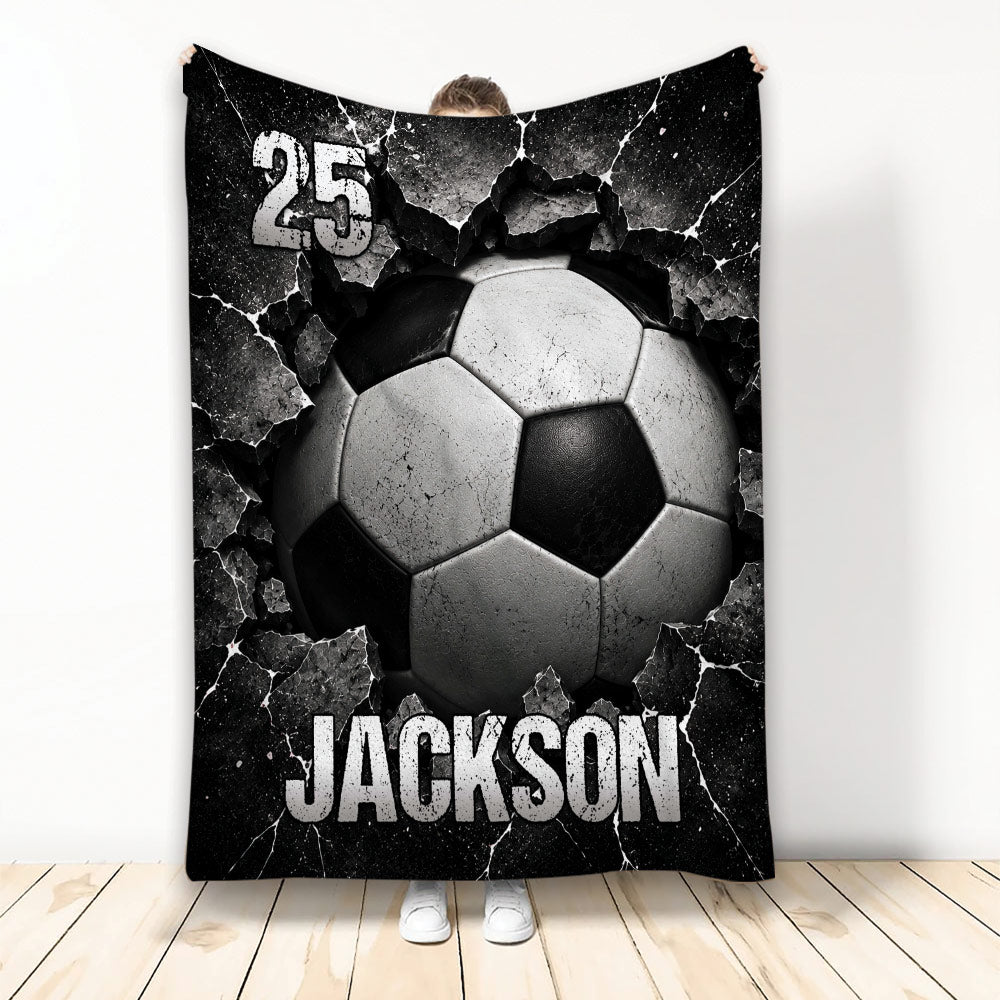 Black and white soccer ball breaking through a cracked surface on a dramatic sports blanket