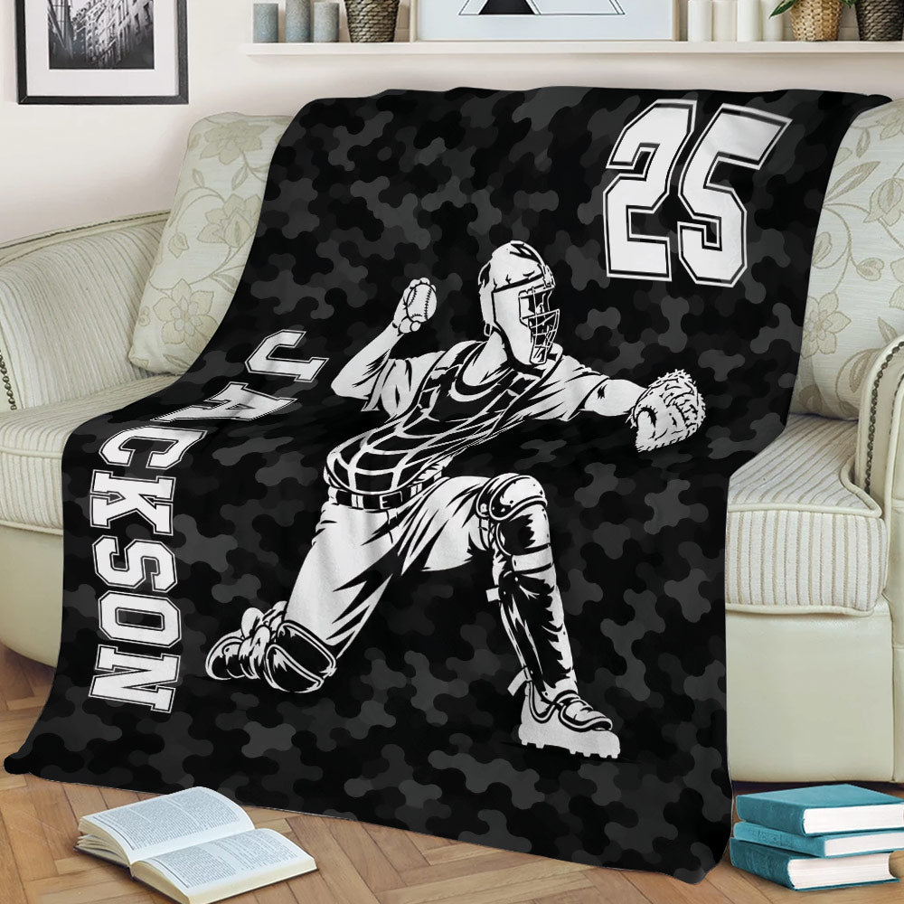 Black camouflage baseball throw blanket featuring a dynamic catcher illustration on a couch