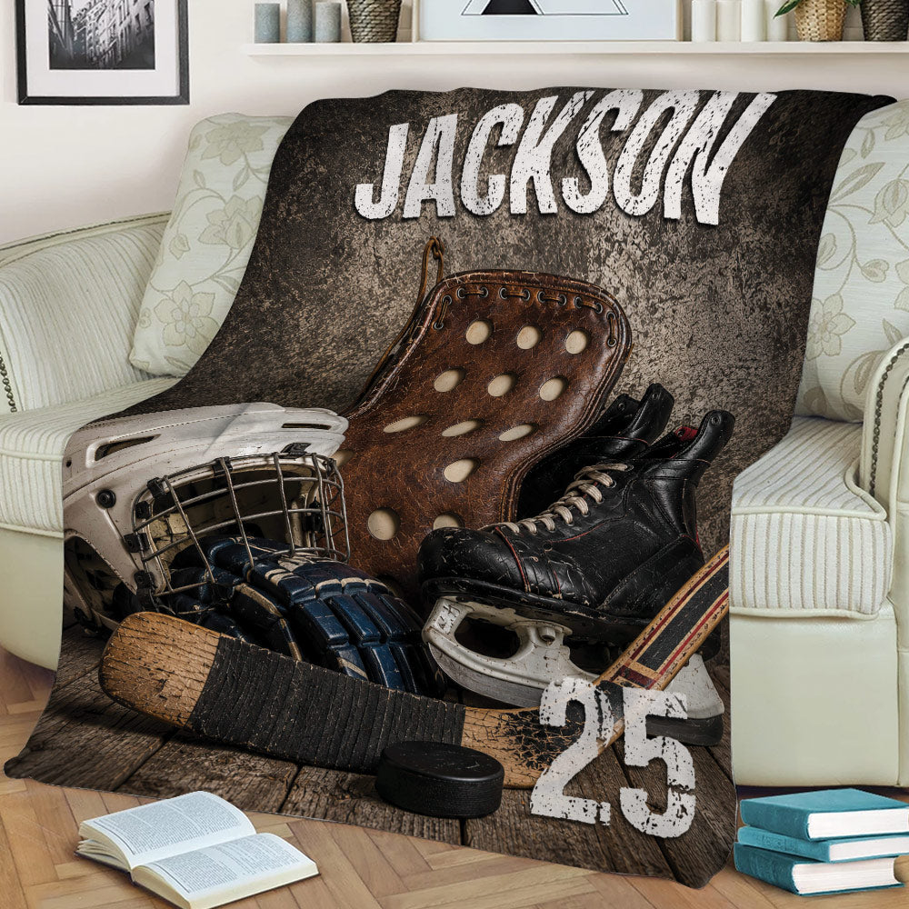 Close view of hockey throw blanket featuring distressed gear artwork, skates, gloves, stick and puck