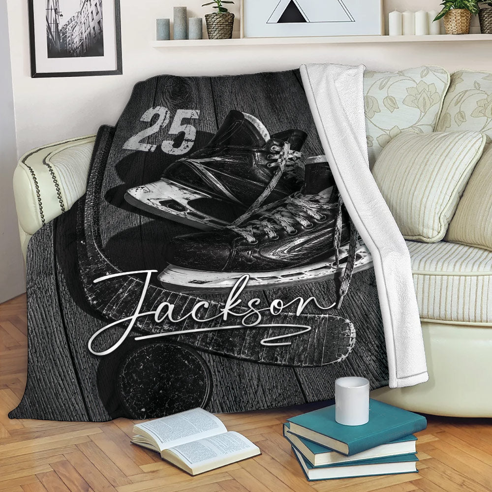 Hockey throw blanket draped over a sofa with black and white skates, hockey stick, puck, and sports artwork