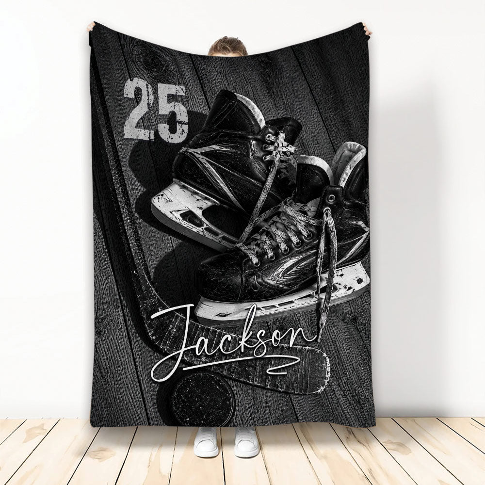 Black and white hockey throw blanket featuring ice hockey skates, a stick, puck, and woodgrain sports artwork