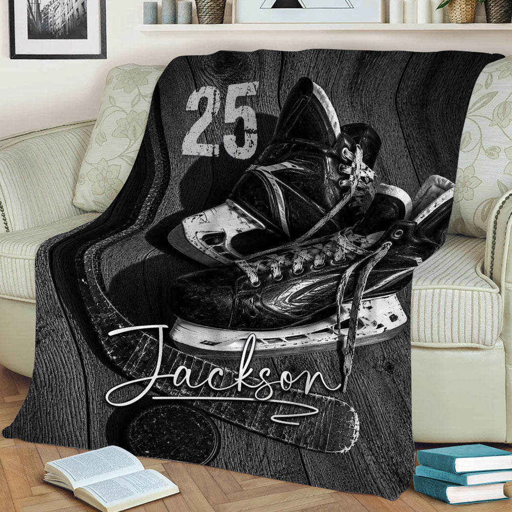 Black and white ice hockey blanket displayed on a couch with skates, stick, puck, and bold sports design