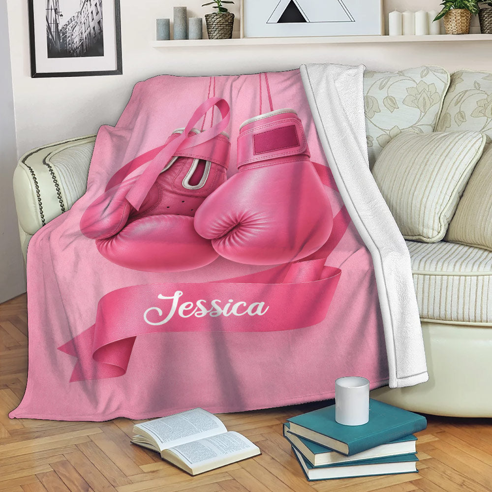 Pink breast cancer awareness blanket displayed on a sofa with boxing gloves and ribbon artwork