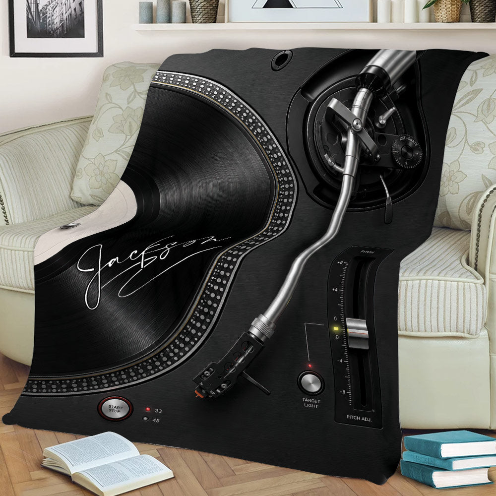 Turntable DJ throw blanket draped across a sofa, featuring black vinyl record and mixer artwork