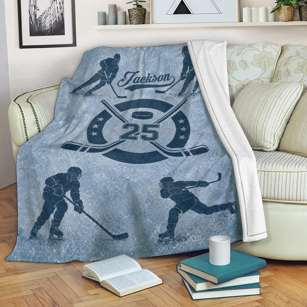 Blue hockey blanket styled on a sofa with illustrated players, crossed sticks, puck, and distressed sports design
