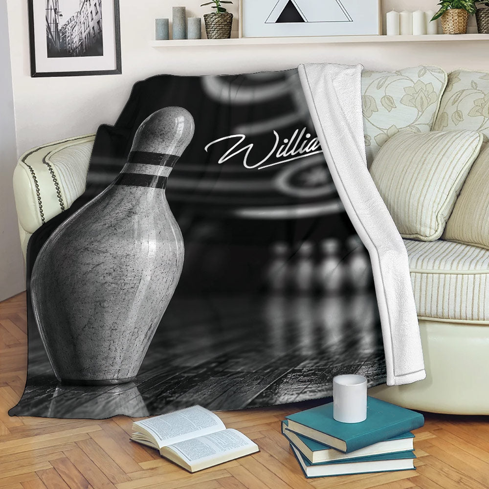 Bowling throw blanket draped over a sofa featuring a metallic bowling pin and dark bowling alley design