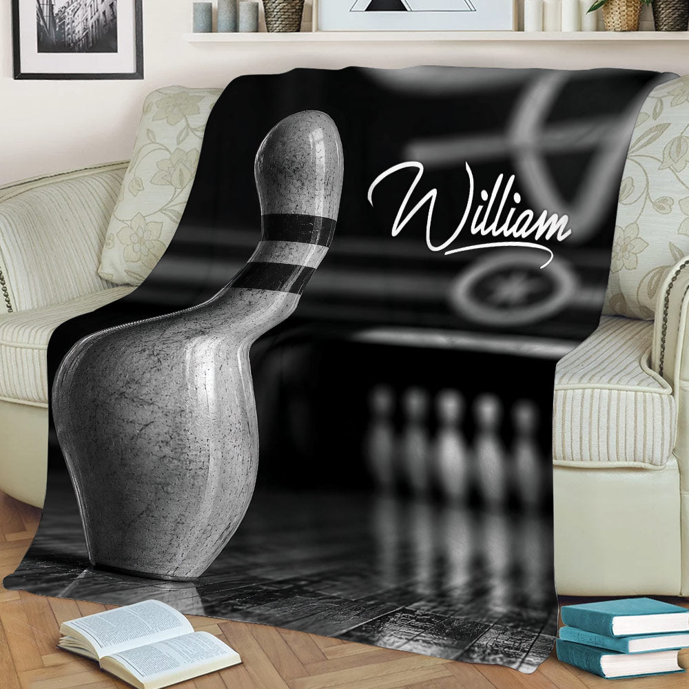 Bowling throw blanket styled on a sofa with bowling pin artwork, lane reflections, and bowling pins in the background