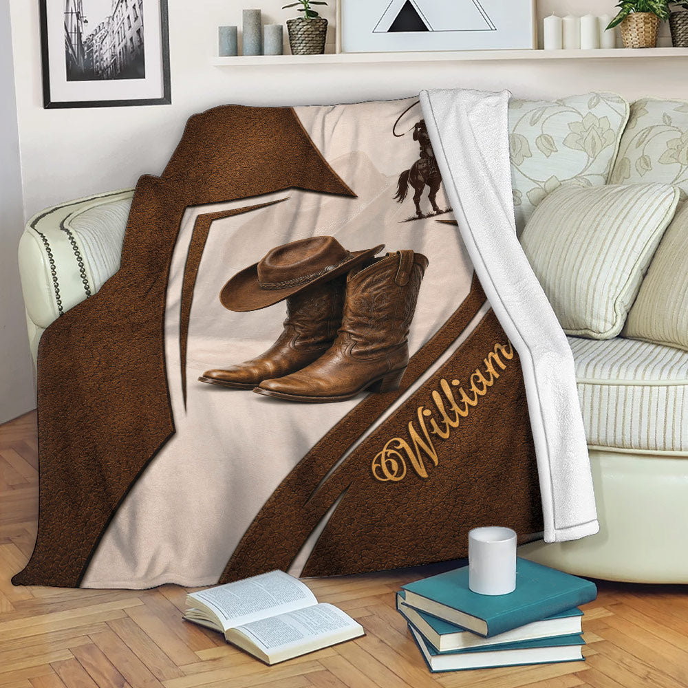 Cowboy blanket draped over a sofa featuring western boots, cowboy hat, horseback rider, and warm rustic artwork